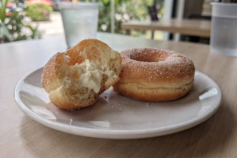 AI illustration: Soft nama-style doughnuts with vanilla custard filling beside a sugar-dusted ring doughnut on a table in natural light