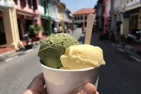 AI illustration: Two scoops of pistachio and mango gelato in a cup on a sunny George Town street