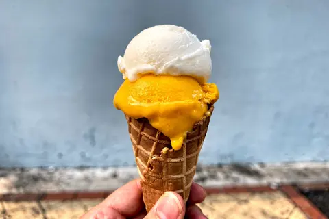 AI illustration: A hand holding a waffle cone with white and yellow gelato outdoors.