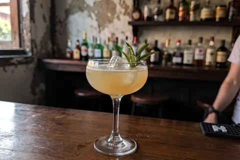 AI illustration: A craft cocktail garnished with fresh herbs on a bar counter in a warm, dimly lit George Town heritage lounge.
