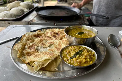 AI illustration: A plate of thin layered roti canai with dhal curry at a Melaka kampung breakfast stall