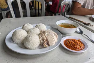 AI illustration: A Melaka chicken rice ball set with hand-rolled rice spheres, sliced poached chicken, chilli-ginger sauce and clear soup in natural light