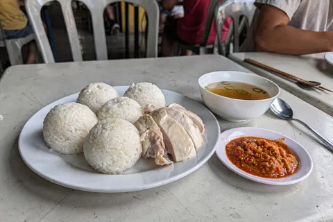 AI illustration: A Melaka chicken rice ball set with hand-rolled rice spheres, sliced poached chicken, chilli-ginger sauce and clear soup in natural light