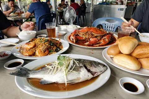 AI illustration: A shared tai-chow seafood spread of whole steamed fish with ginger and soy, chilli crab with mantou and butter prawns on a restaurant table.