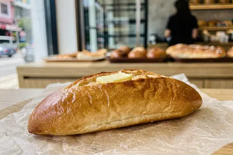 AI illustration: A glossy golden shio pan roll with a melting butter cavity on parchment paper at a bakery counter