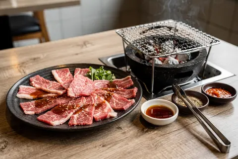AI illustration: Sliced raw beef cuts on a plate beside a small charcoal yakiniku table grill in natural light