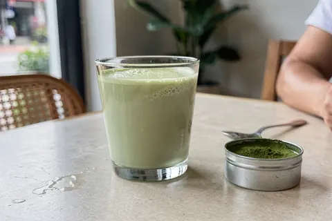 AI illustration: A vibrant milky green matcha latte served in a glass on a cafe table in natural light.