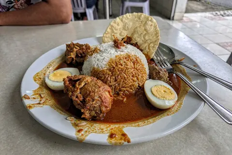 AI illustration: A plate of banjir-style nasi kandar with rice flooded in mixed curries, fried chicken, hard-boiled egg and papadam.