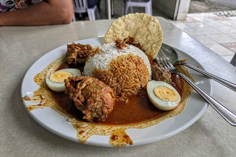 AI illustration: A plate of banjir-style nasi kandar with rice flooded in mixed curries, fried chicken, hard-boiled egg and papadam.