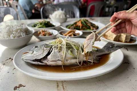 AI illustration: Steamed fish topped with ginger and scallion in soy broth, a classic tai chow seafood dish served family-style in Ipoh.