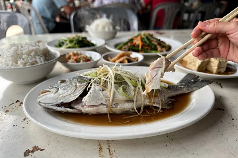 AI illustration: Steamed fish topped with ginger and scallion in soy broth, a classic tai chow seafood dish served family-style in Ipoh.