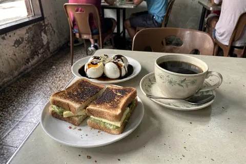 AI illustration: Charcoal kaya toast, half-boiled eggs with soy sauce and a cup of kopi O on a kopitiam table